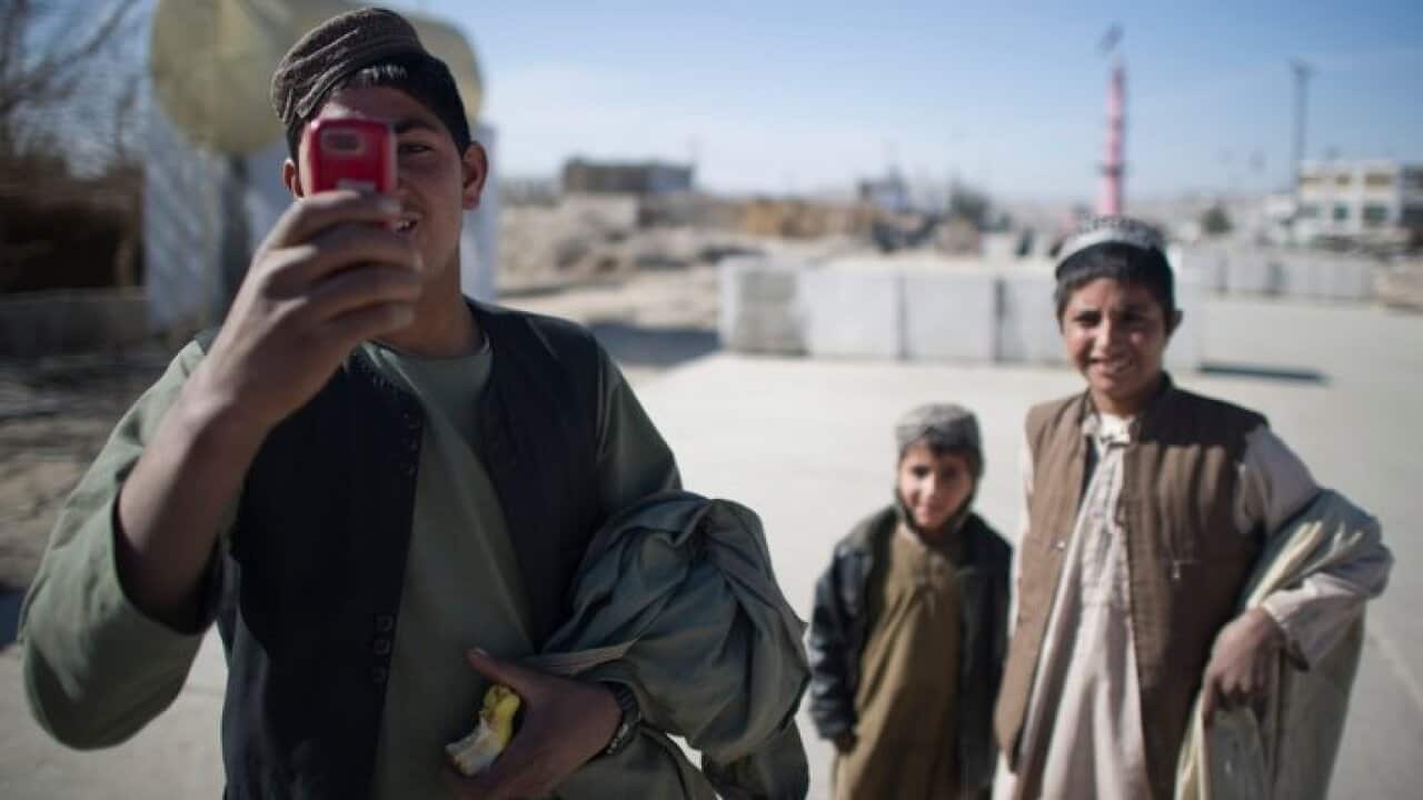 An Afghan youth uses his mobile phone to