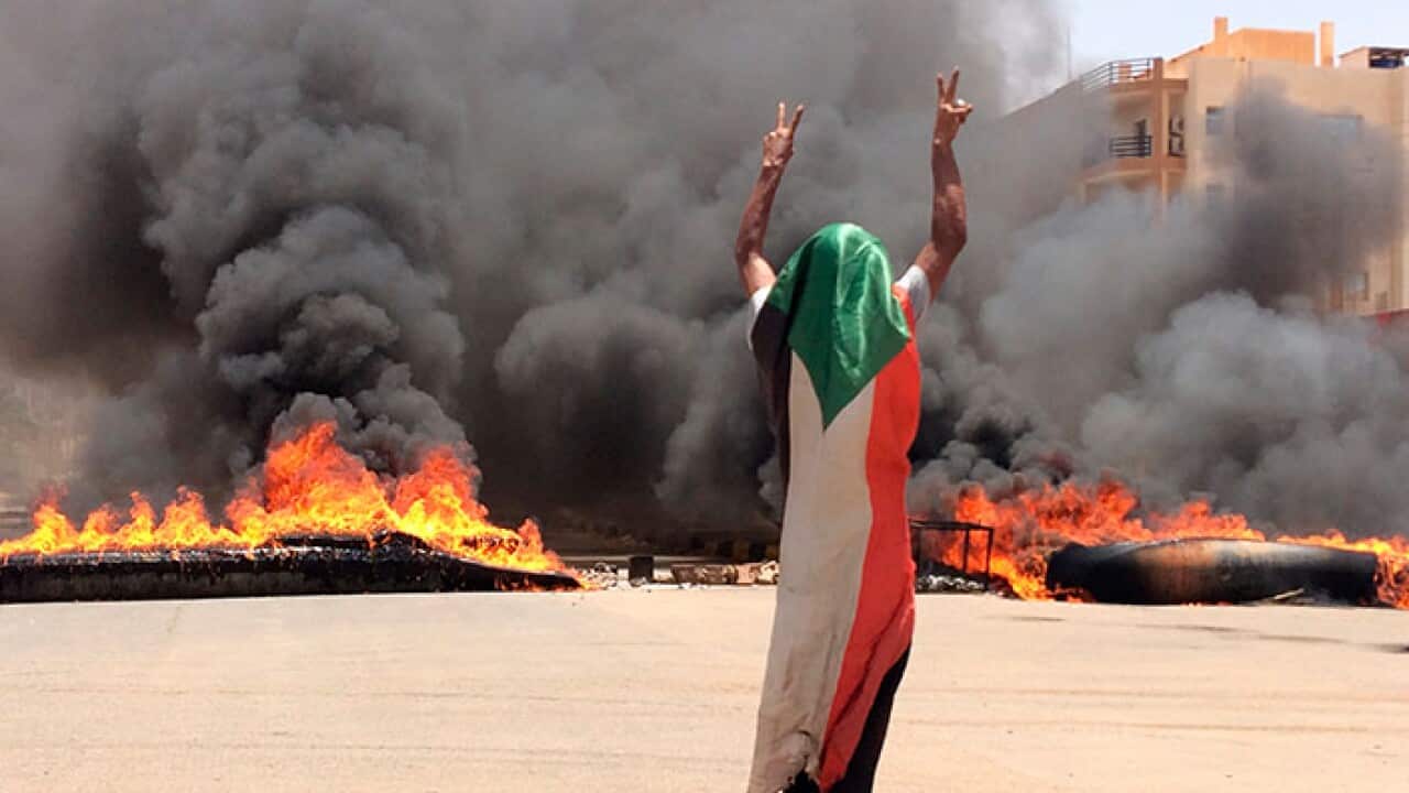 A protester wearing a Sudanese flag flashes the victory sign in front of burning tires and debris near Khartoum's army headquarters