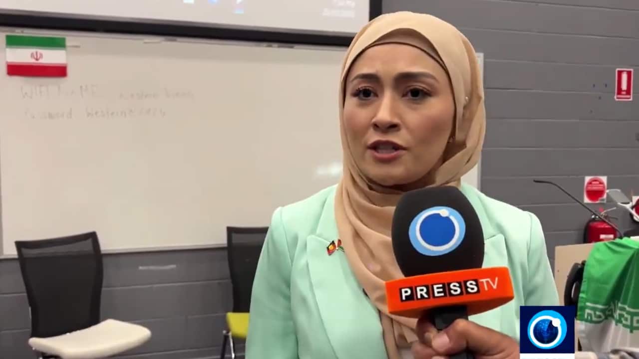 A woman wearing a mauve hijab speaks into a press microphone