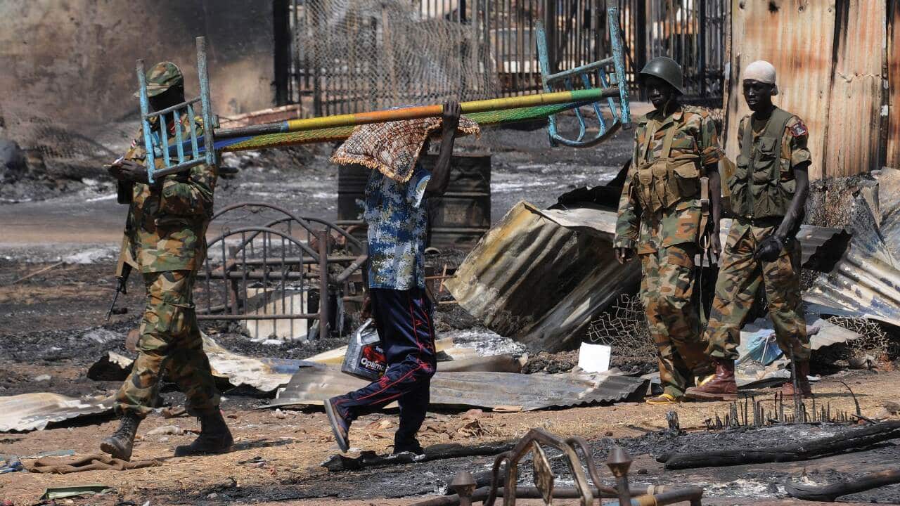 A man carrying a bed past government soldiers in Bentiu (AAP).jpg