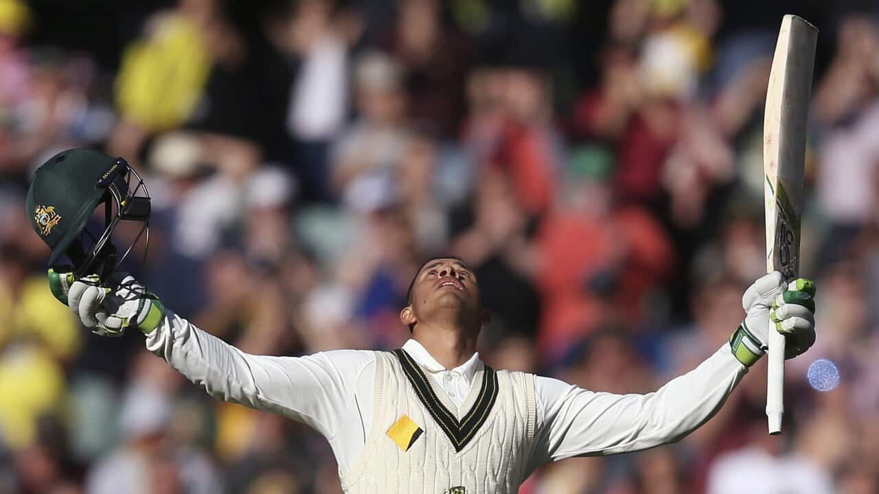 Usman Khawaja lifts his helmet and cricket bat.