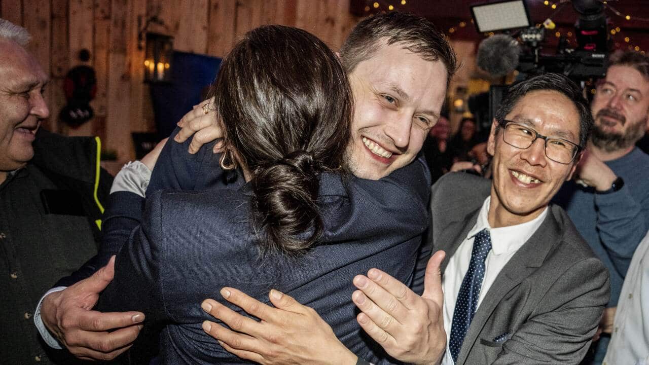 A man in a suit smiles as he hugs a woman, surrounded by supporters.