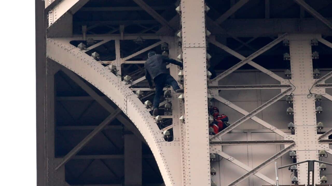 A man (L) climbs the Eiffel Tower while firemen attempt to stop him in Paris, France, 20 May 2019 (AAP)
