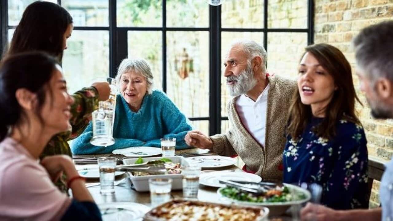 Extended family sitting round dinner table chatting and eating dinner