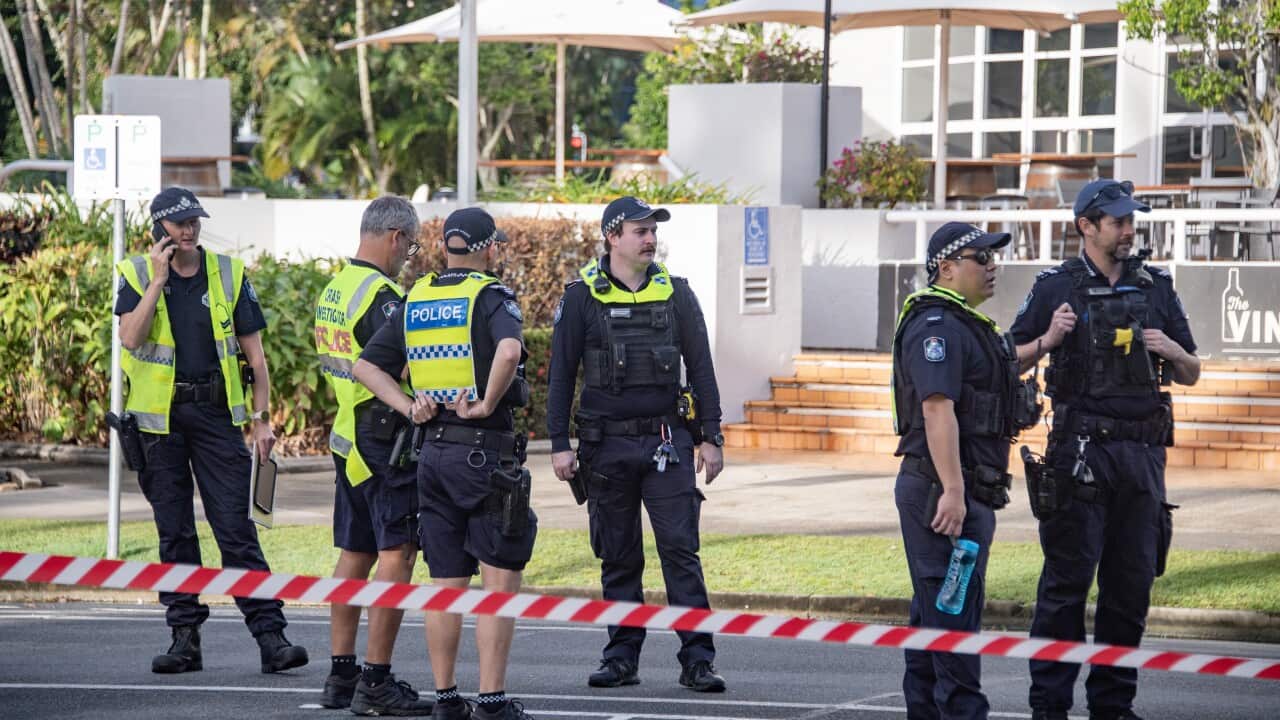 Several police standing behind white and red tape. A white hotel is in the background.
