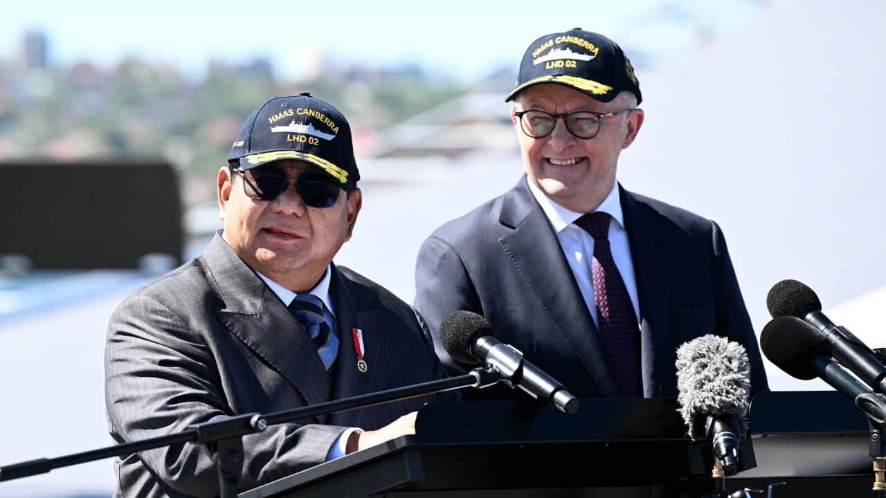 Two men in suits and caps reading HMAS Canberra standing together at a lectern outside