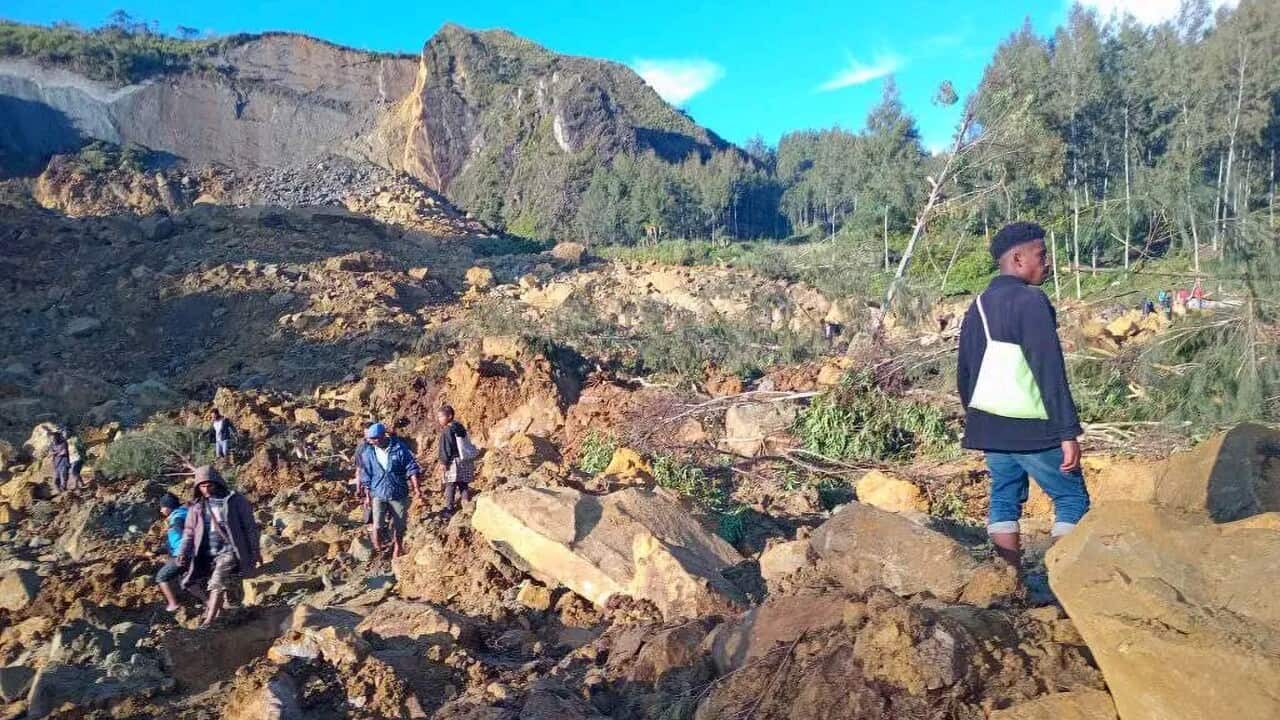 A couple of people scan an area hit by a landslide.