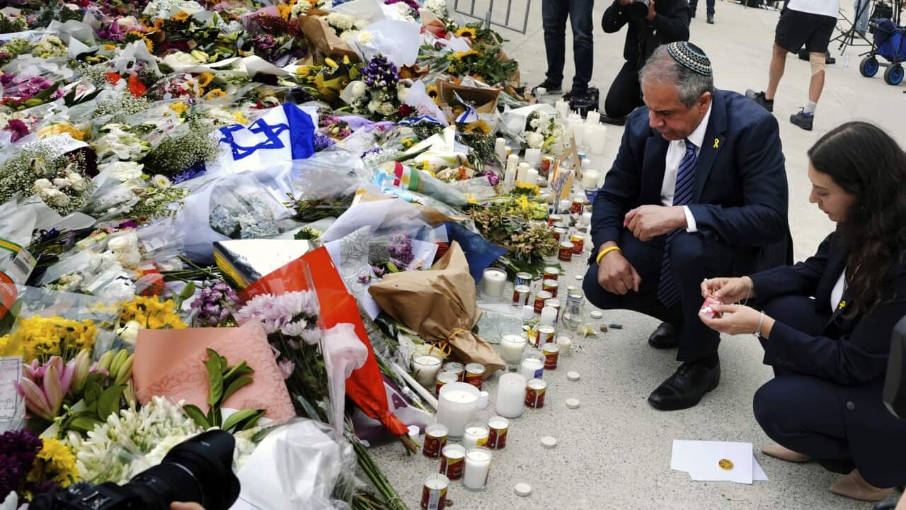 A man and woman kneeling beside floral tributes.