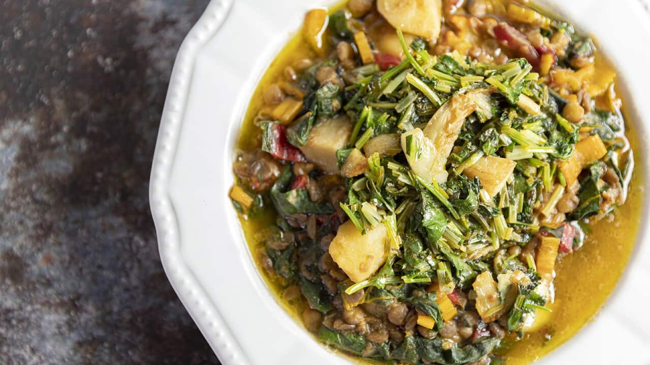 A soupy lentil, potato and coriader mixture sits in a white bowl with a wide rim.