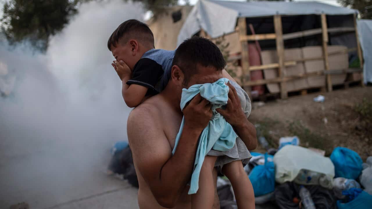 A man holds a boy and protects himself from tear gas during clashes with police outside the refugee camp of Moria on the Greek island of Lesbos