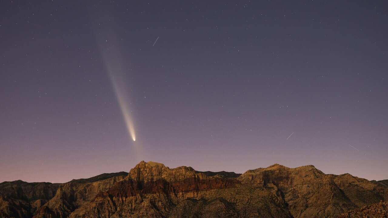 A comet streaks through a dark blue and purple sky with rugged mountains visible below.
