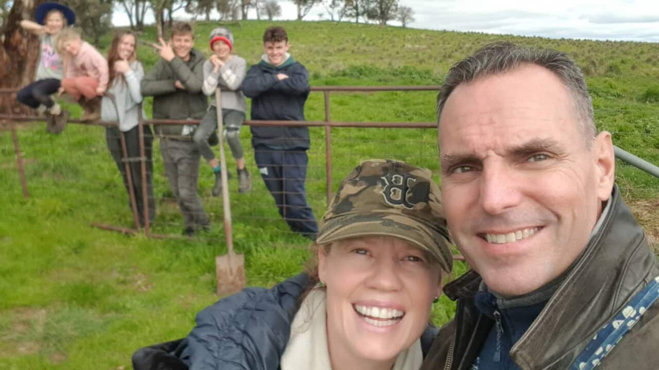 A couple takes a selfie with a group of people in the background.
