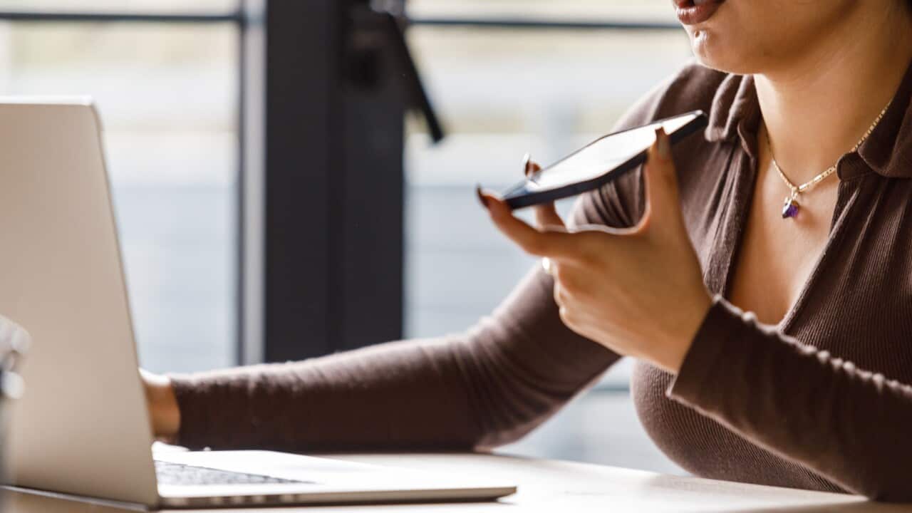 Young woman using laptop and talking on the phone via speakerphone