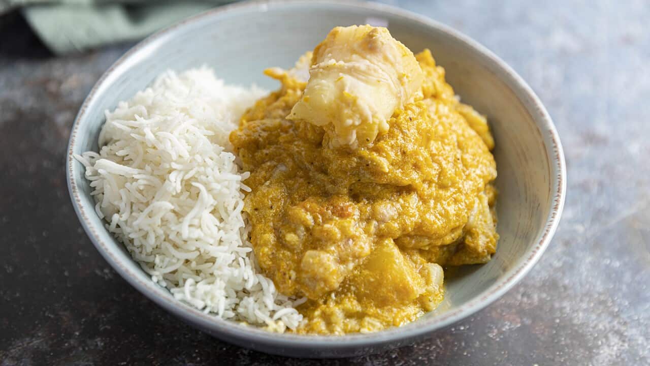 A thick yellowish stew with large chunks of vegetable sits in a wide bowl, along with cooked white rice.