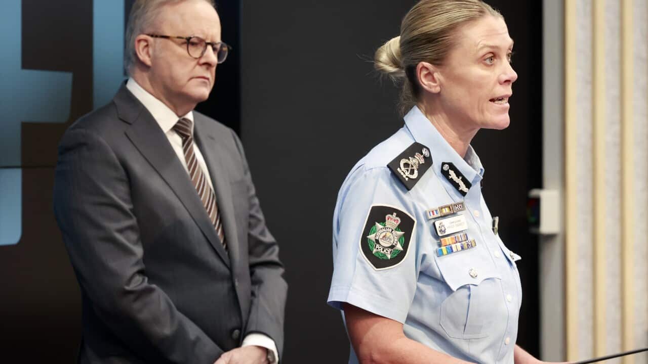 Anthony Albanese in a black suit standing behind Krissy Barrett, who is wearing a blue police uniform and speaking at a lectern.