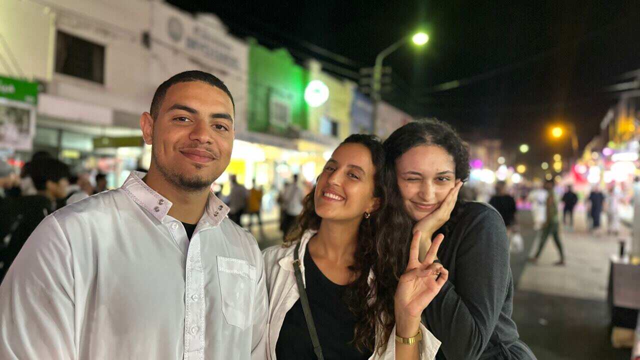 A man and two girls pose on a street at night. 