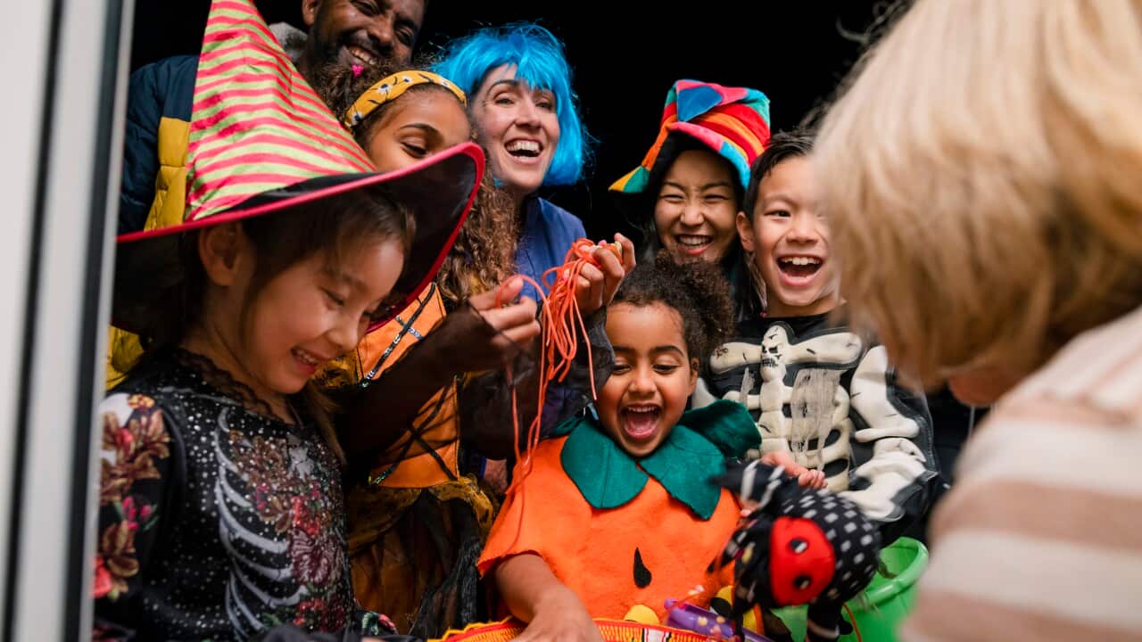Children in costumes grabbing candy at a doorway.