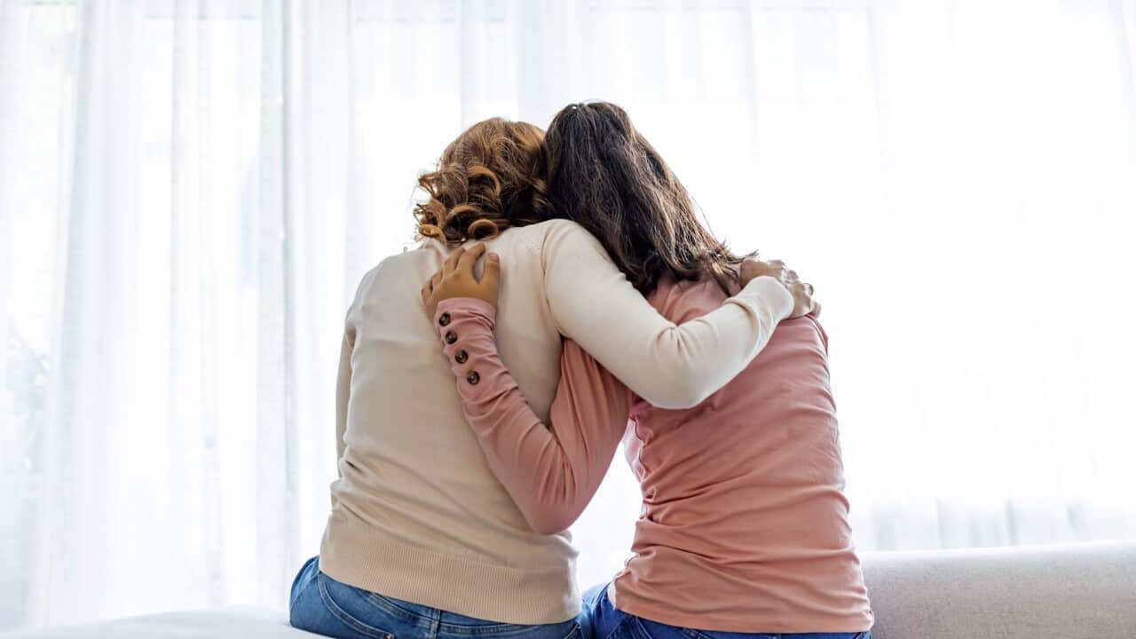 Rear view of mother and daughter embracing sitting on bed