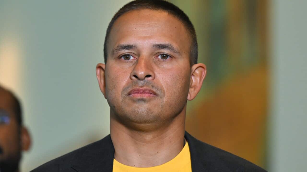 A man in a blue jacket worn over a yellow round-neck t-shirt.