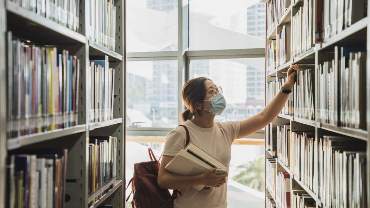 adult student wearing face mask looking at the books from the bookshelf