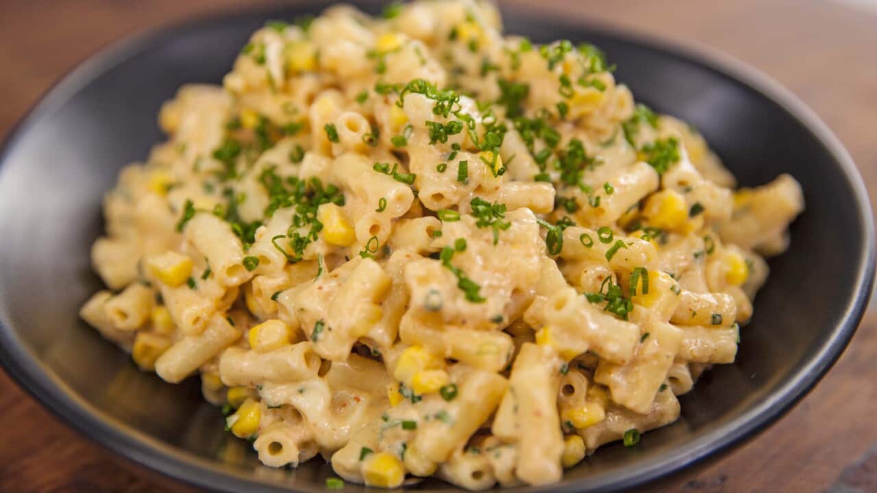 A dark bowl holds macaroni in a creamy sauce, studded with corn kernals.