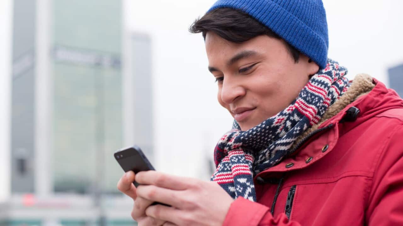 Smiling man using cell phone in city during winter