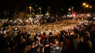 People form a circle around flowers and other tributes at a vigil.