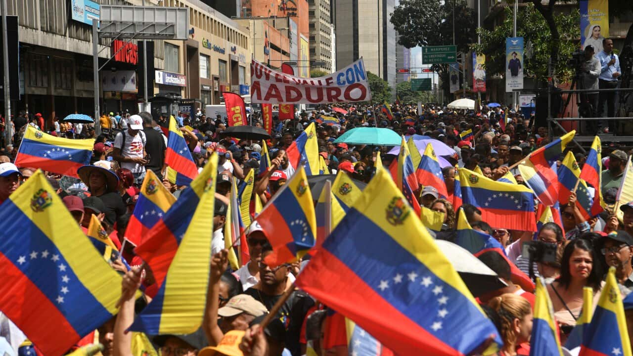 A large crowd of people walking down a street, waving Venezuelan flags.