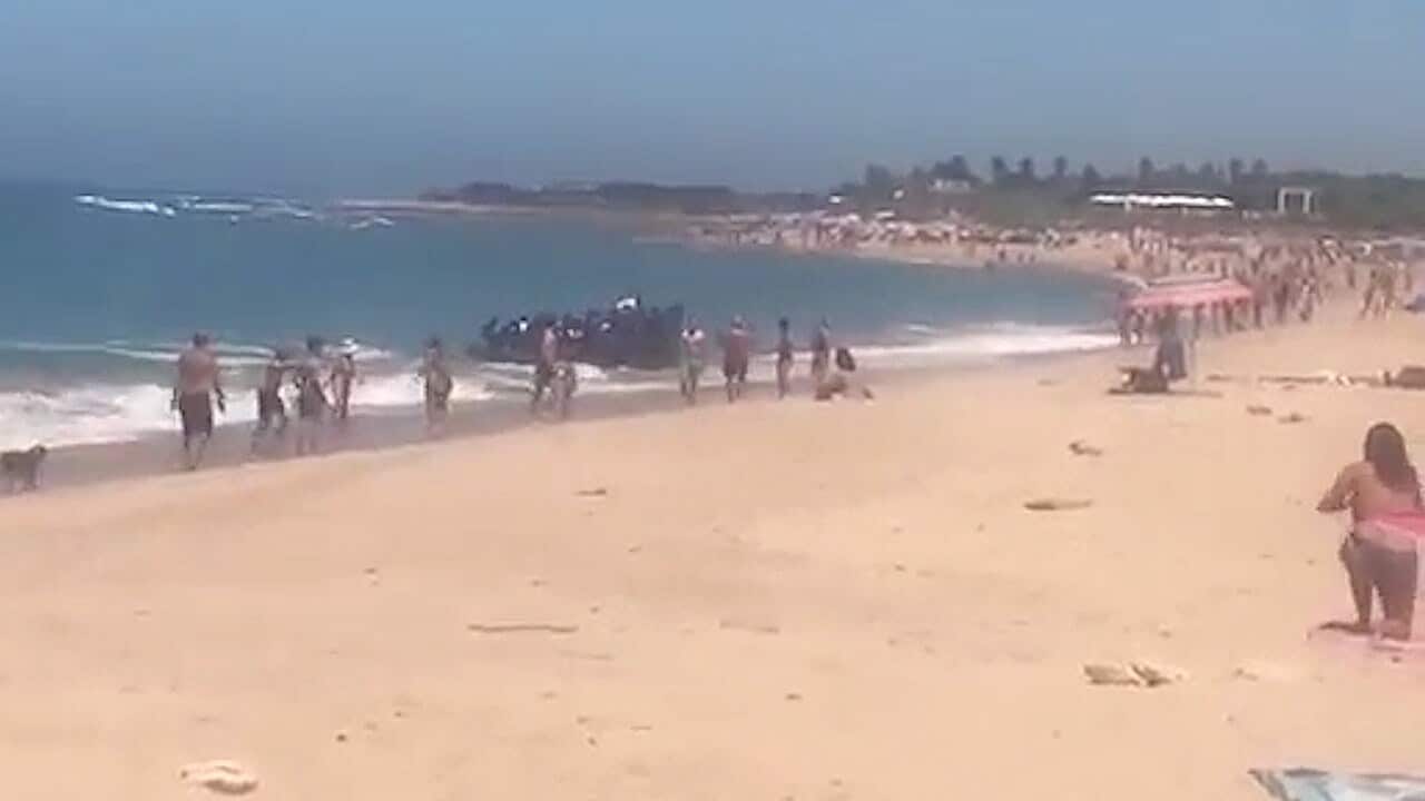 Holiday makers looked on as dozens of migrants land on a beach in Spain.