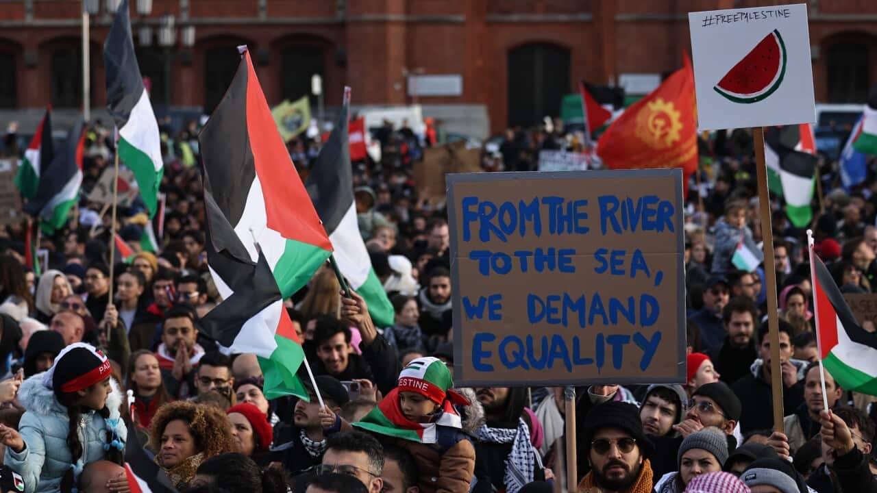 People protest at a rally, with one person holding a placard reading 'From the river to the sea, we demand equality'