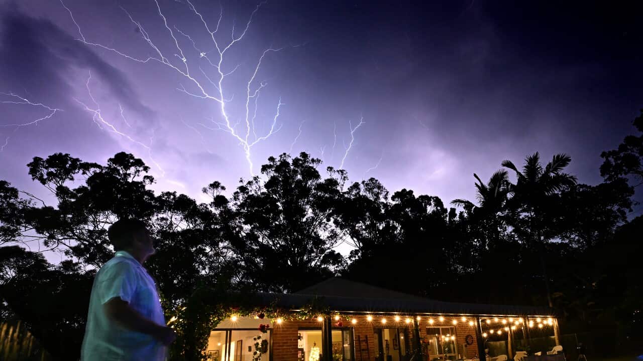 A woman looks up at a purple sky with white thunder lightning.