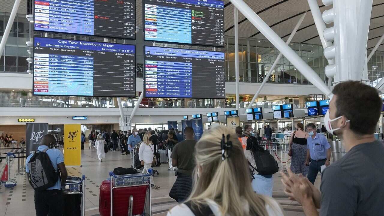 Travellers look at a flight information notice board at Cape Town International Airport as restrictions on international flights take effect 28 Nov 2021.