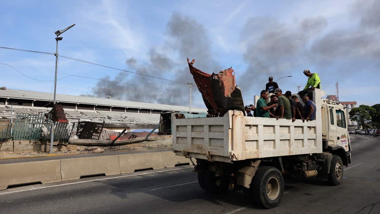 People sit in a truck as it drives down a road in Venezuela. Smoke plumes can be seen in the distance.