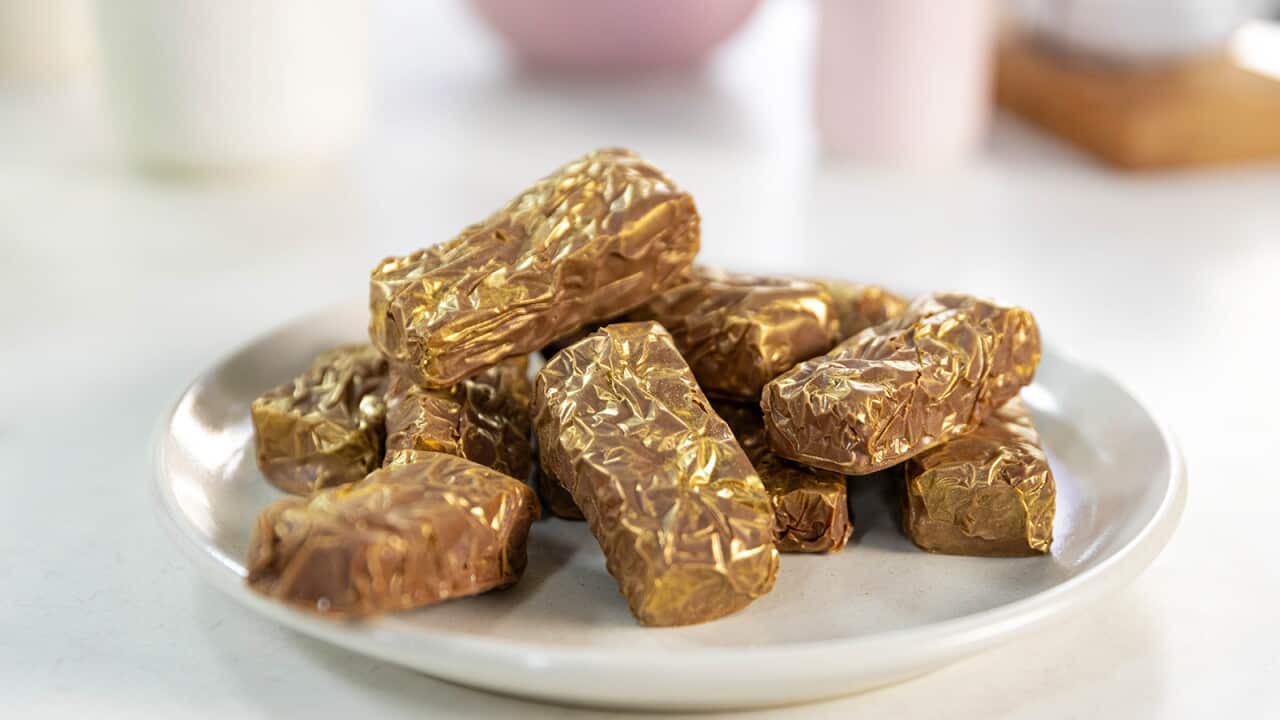 A pile of chocolate-coated bars sit on a round white plate. The bars glean with hints of gold.