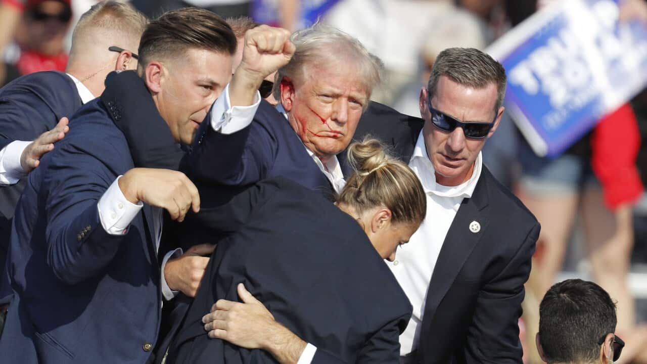 Former US President Donald Trump with blood on his face and surrounded by security staff.