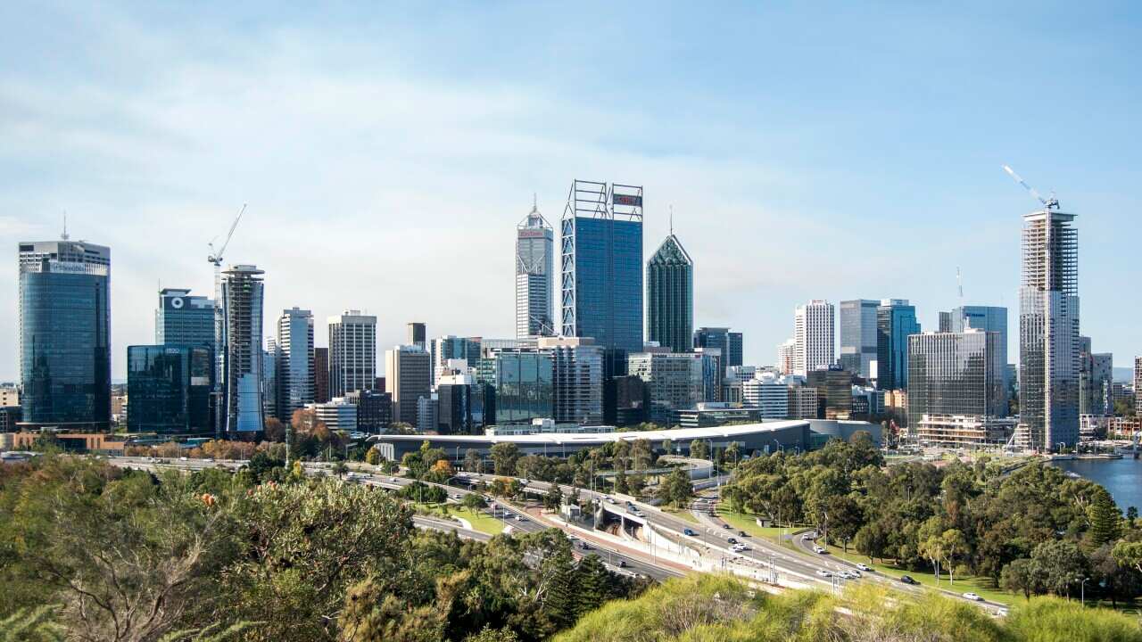 A skyscraper skyline fronted by parkland areas besides an arterial road seen during the day.