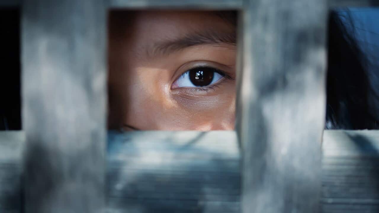 The blank stare of a child's eye who is standing behind what appears to be a wooden frame