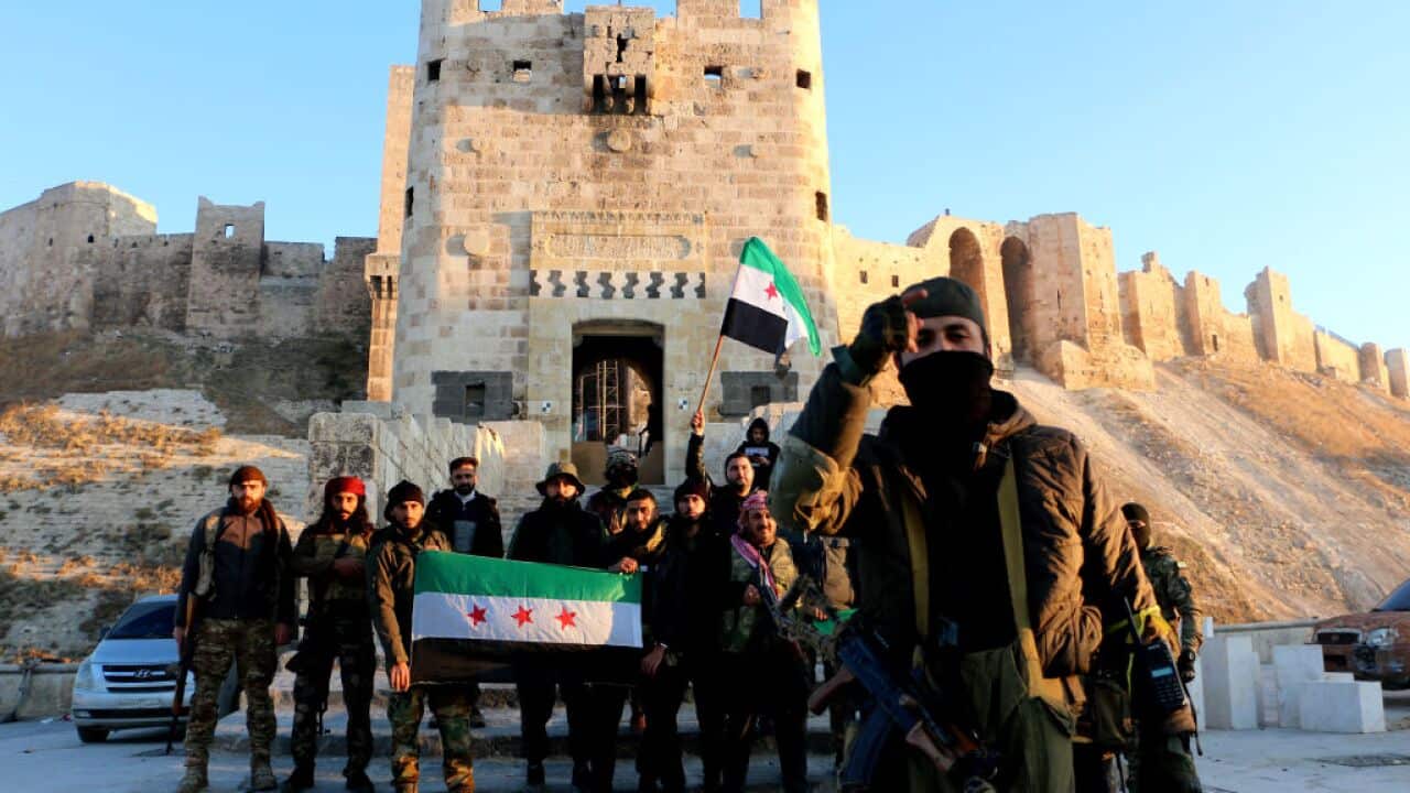A group of men with a flag standing in front of an old fort-style building