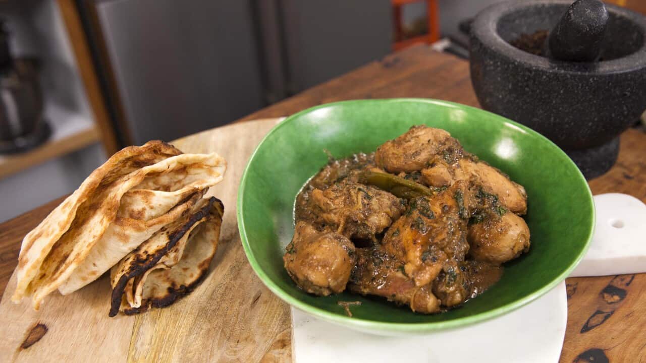 A green bowl holds a dark chicken dish. Fresh folded flatbreads with dark edges sit alongside.