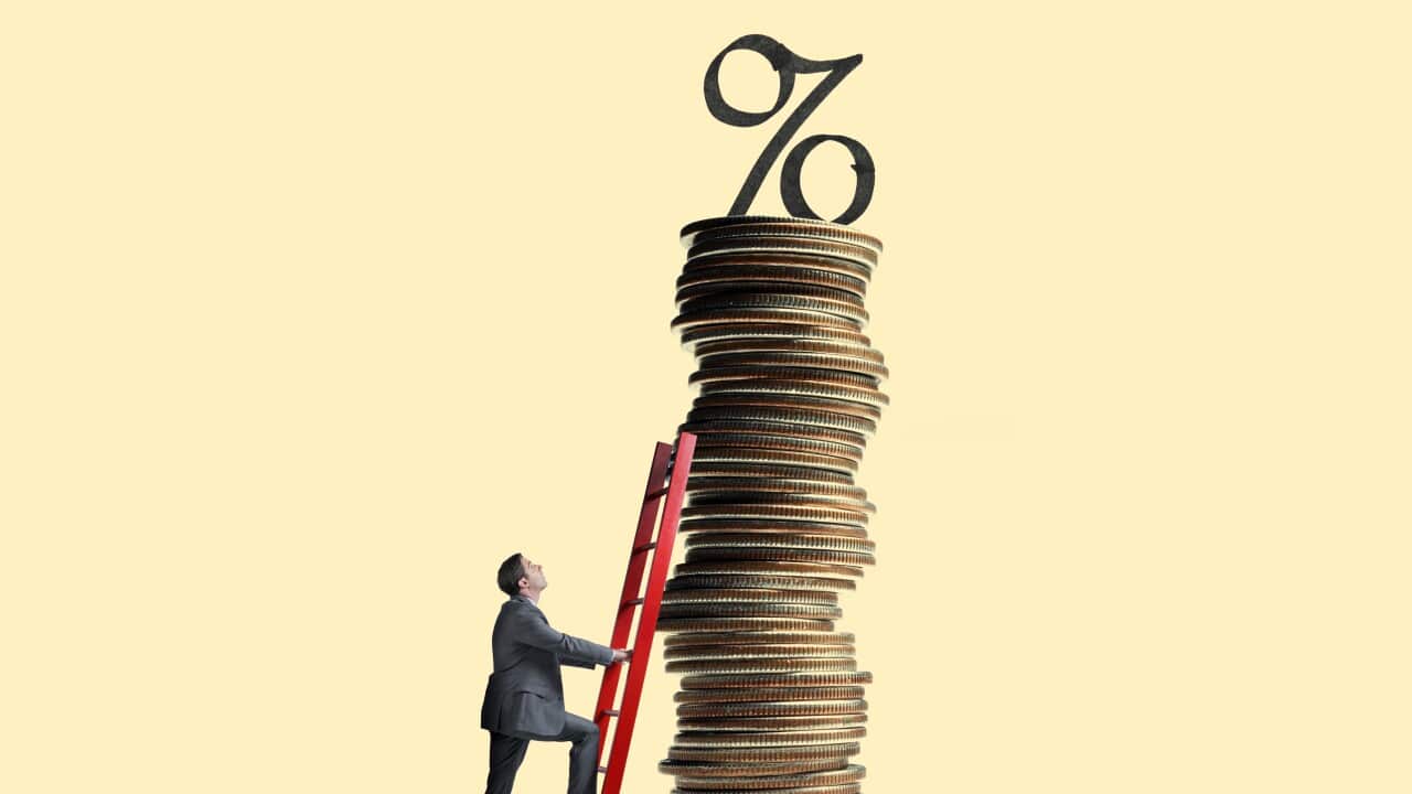 Man Leans Ladder Against Tall Stack Of Coins Topped With Interest Rate Symbol