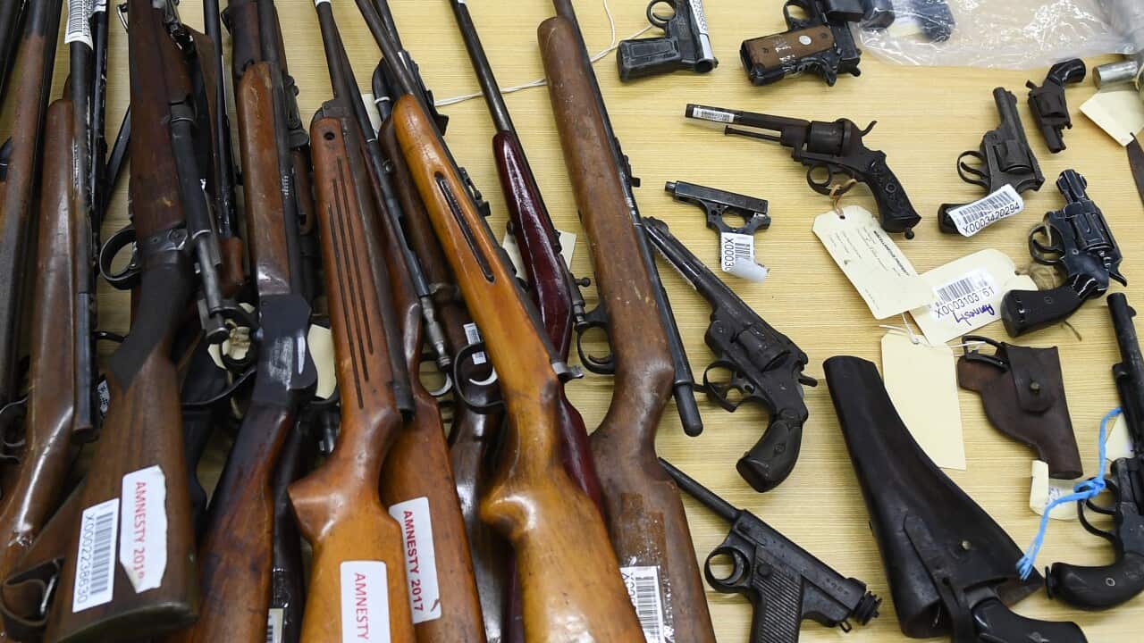 A collection of various firearms, including rifles and handguns, laid out on a table. Some of the long guns have tags on them.