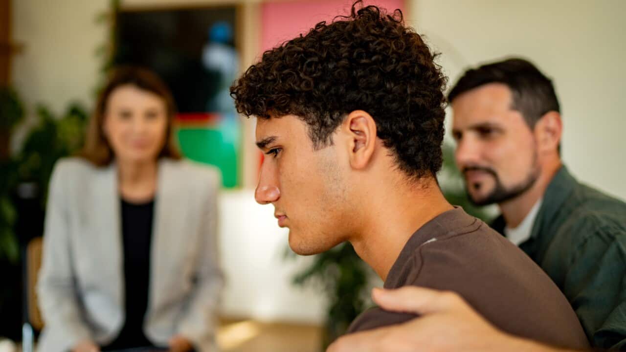 Teenage boy being comforted by father during psychotherapy session