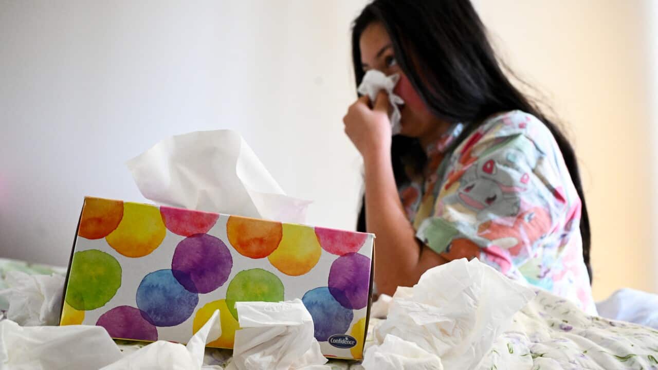 A girl blowing her nose in the background of a tissue box
