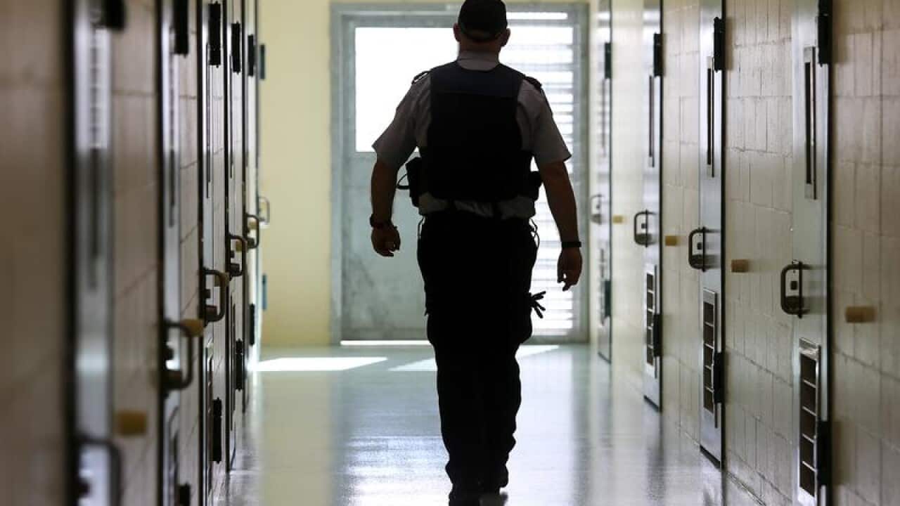 A corrections officer walks down a cell corridor.