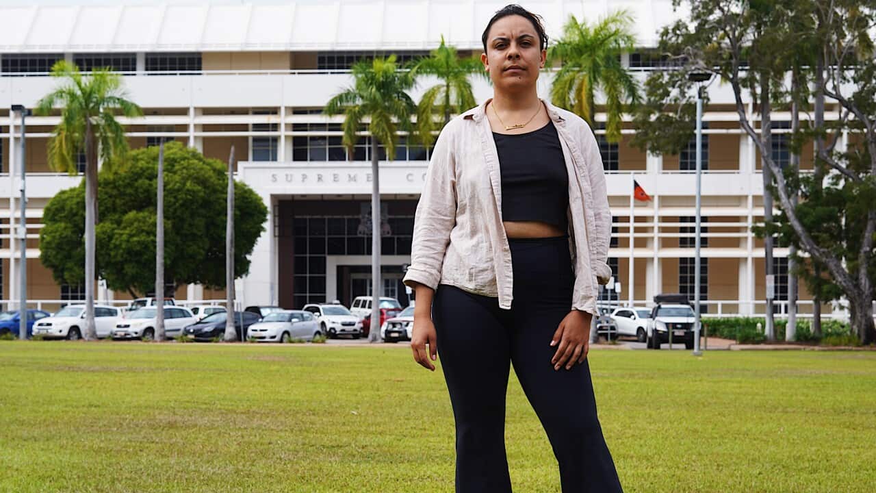 A woman standing on grass with a building in the background.