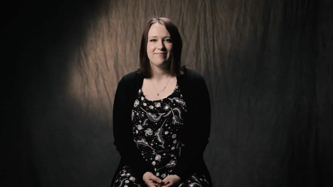 A woman with short hair in a black cardigan smiles at the camera.