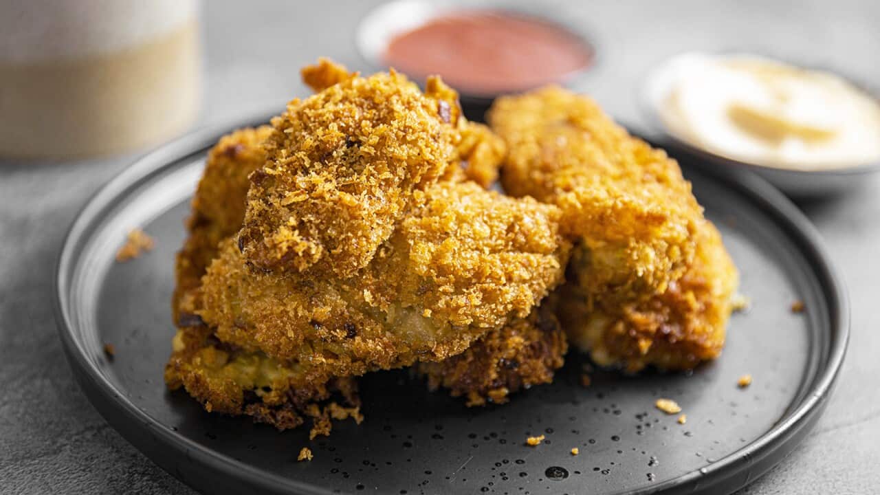 Unevenly shaped golden breadcrumb-covered croquettes sit on a plate. Small bowls of sauce can be seen behind.