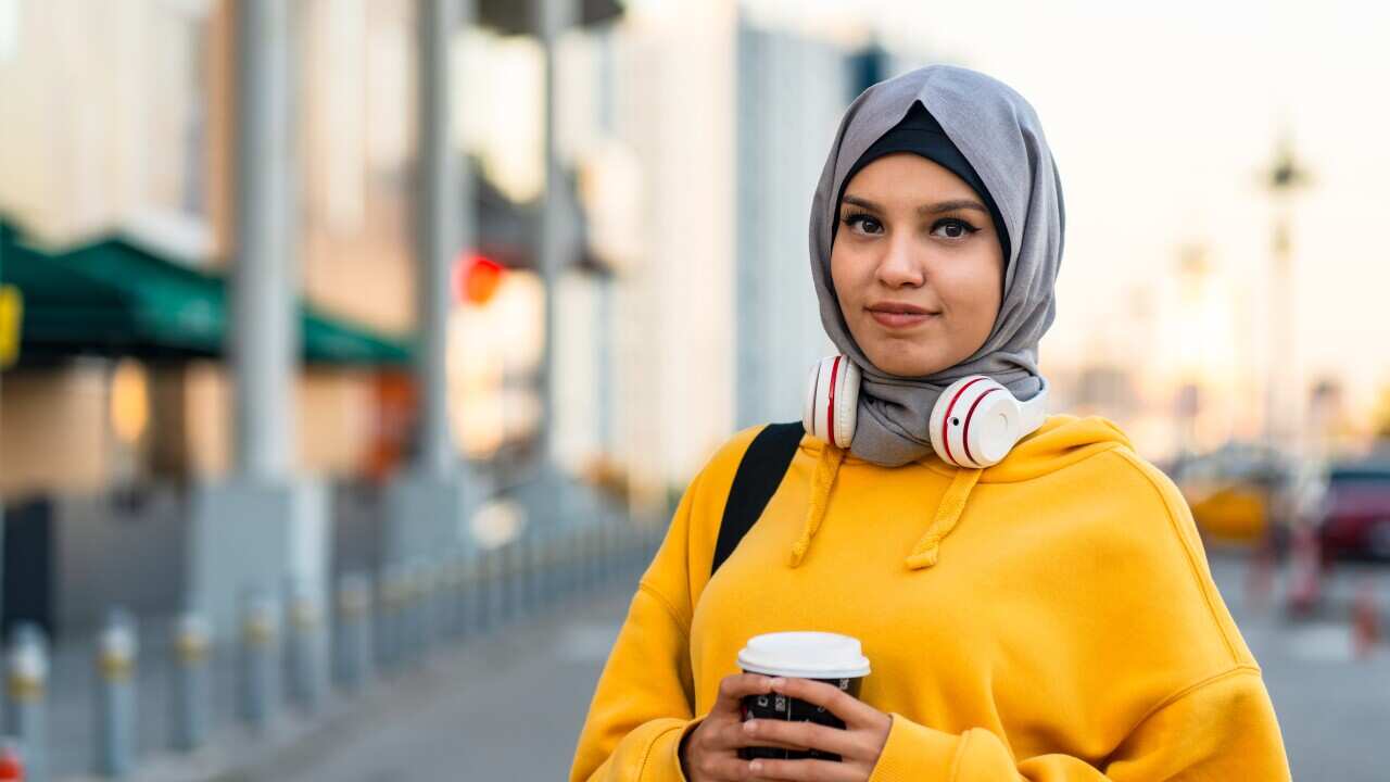 Stock photo of a young woman wearing a headscarf and holding a coffee cup