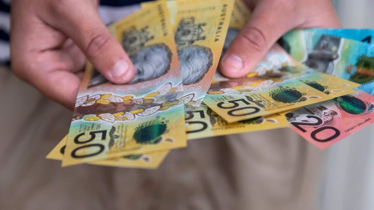 A pair of hands holding an assortment of Australian cash