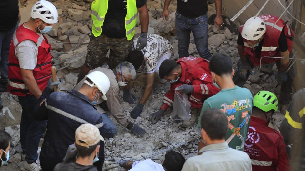Rescue workers, some wearing hard hats, are searching through the rubble.
